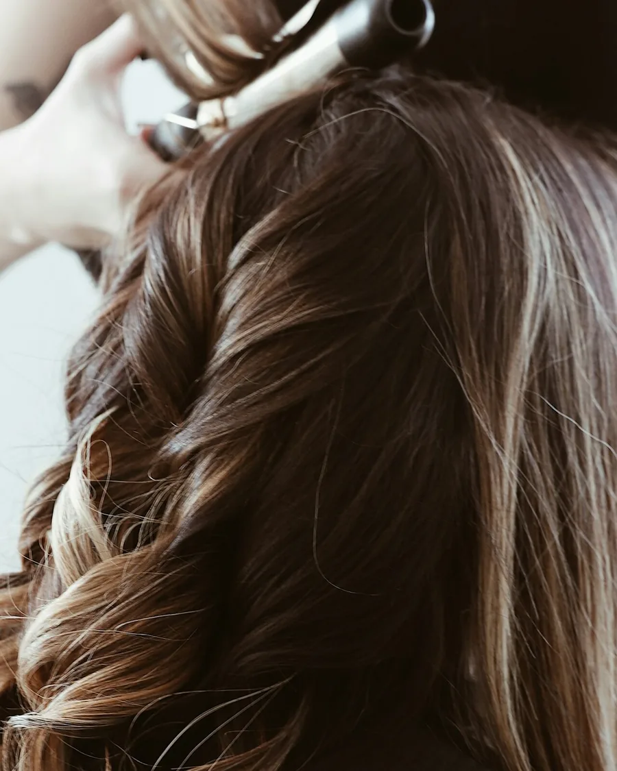 Cabelo visto de costas sendo finalizado com prancha, mecha a mecha