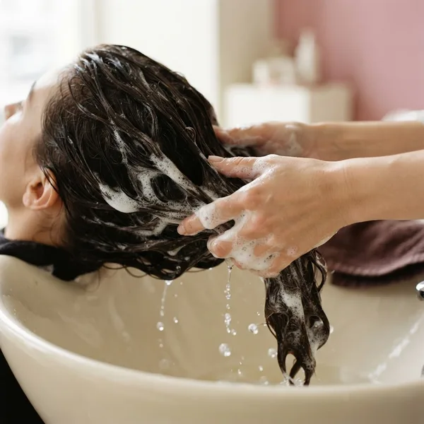 Mãos com espuma de shampoo massageando o cabelo molhado na pia